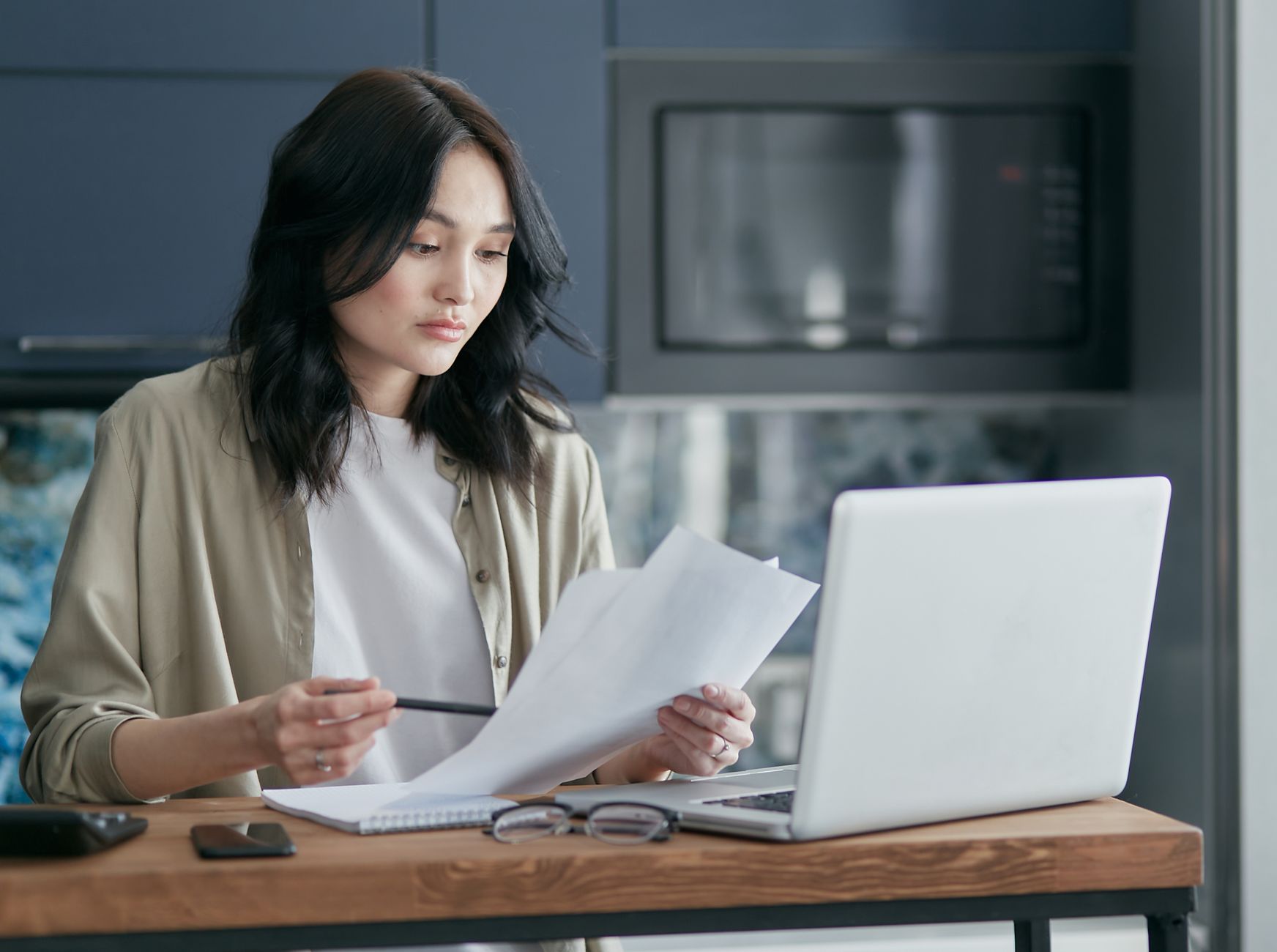 Person reading a printed document beside a laptop at a desk